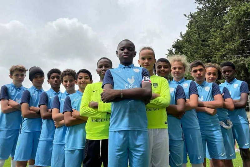 Monimuotoinen nuorten jalkapallojoukkue poseeraa itsevarmasti Välimeren Jalkapallicupissa.