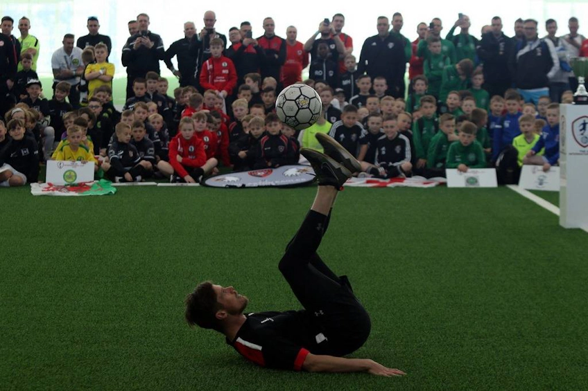 Fotbalist efectuând o foarfecă în fața tinerilor participanți la UK International Cup
