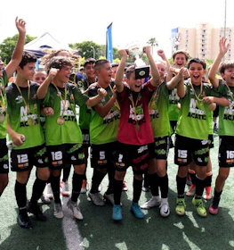 Ausgelassenes Jugendfußballteam mit Pokal feiert Sieg beim Mallorca International Football Cup.