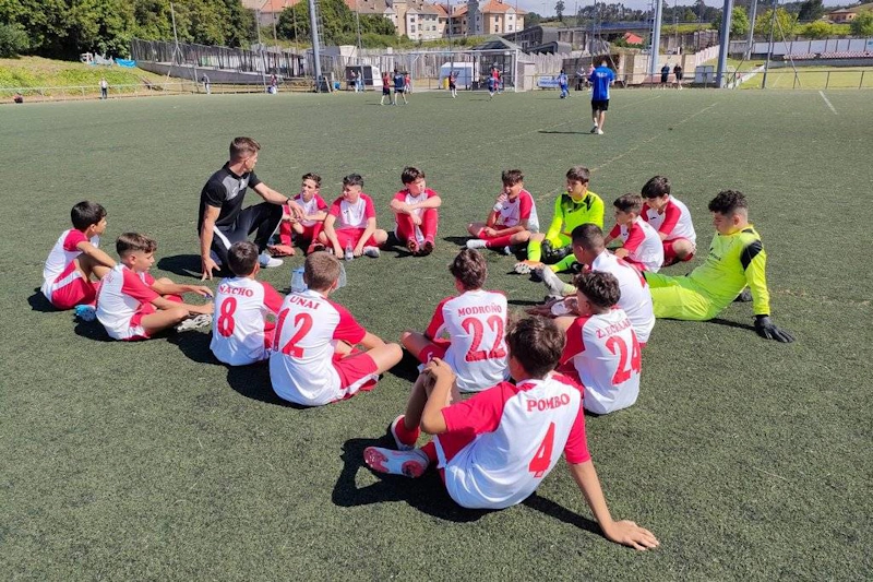 필드에서 빨간색과 하얀색 유니폼을 입은 젊은 선수들과 전략을 논의하는 축구 코치.
