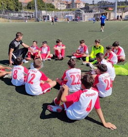 Football coach discussing strategy with young players in red and white kits on the field.