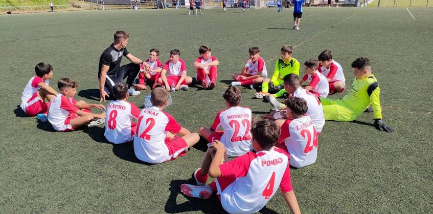 Football coach discussing strategy with young players in red and white kits on the field.