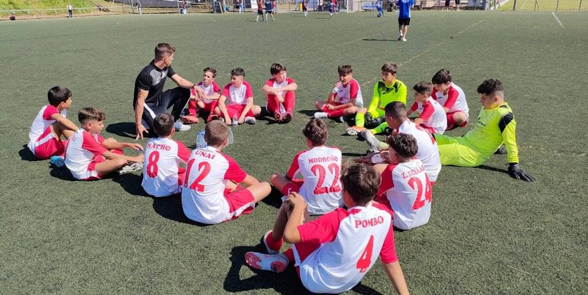 Soccer coach discussing tactics with young players in red and white uniforms on the pitch.