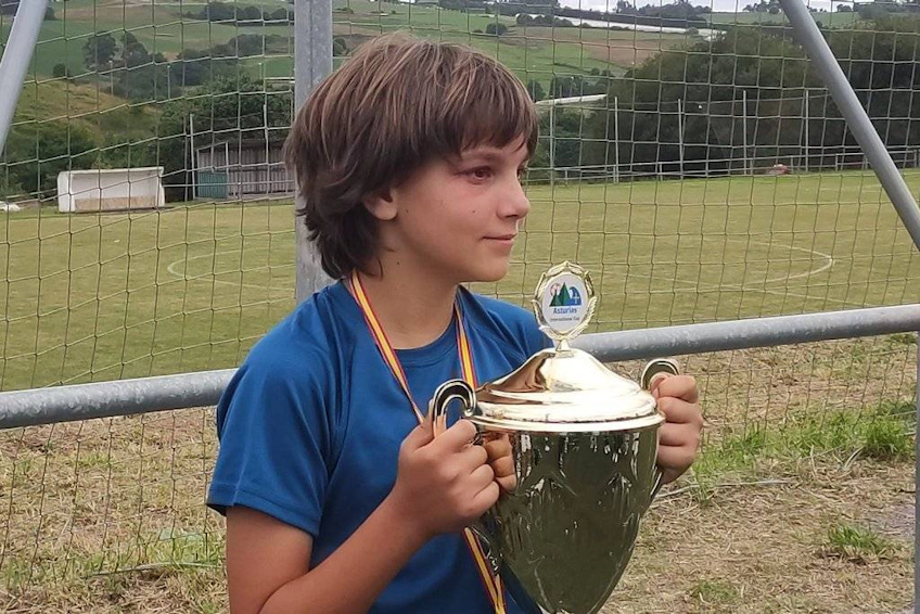 Joven jugador sosteniendo un trofeo en el campo de fútbol de la Copa Internacional de Asturias