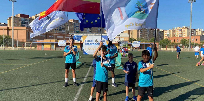 Młodzi piłkarze z flagami Hiszpanii i Unii Europejskiej na boisku.