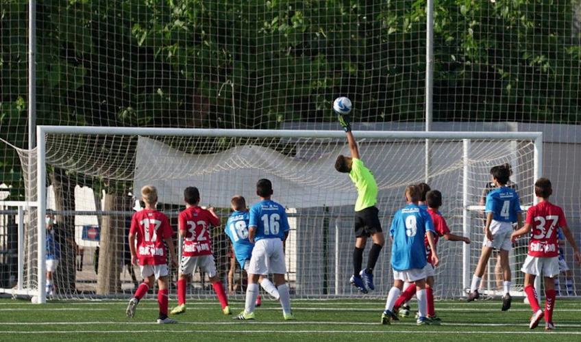 Giovane portiere in verde salta per salvare un gol durante una partita di calcio giovanile.