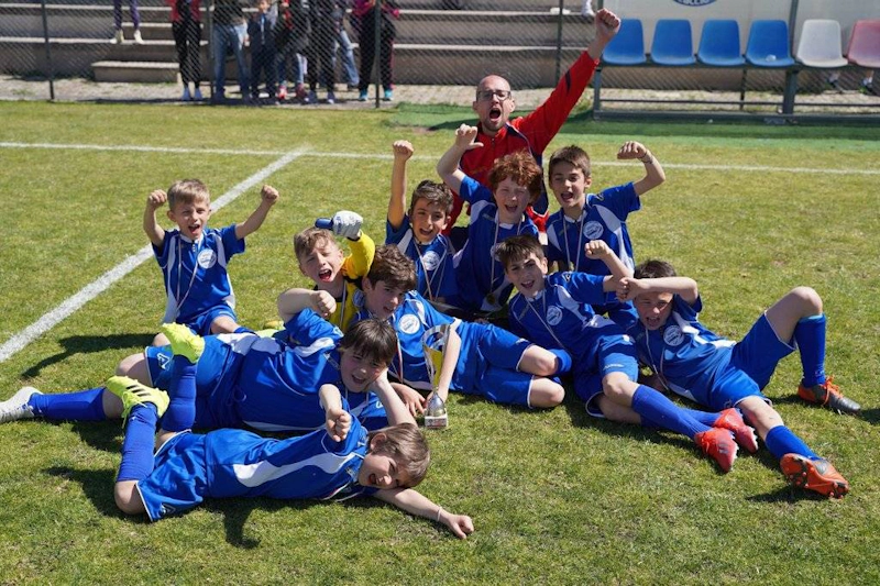 Glad ungdomsfotballag i blått feirer en seier på banen på Roma International Cup.