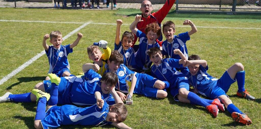 Joyful youth soccer team in blue celebrating a victory on the field at the Roma International Cup.