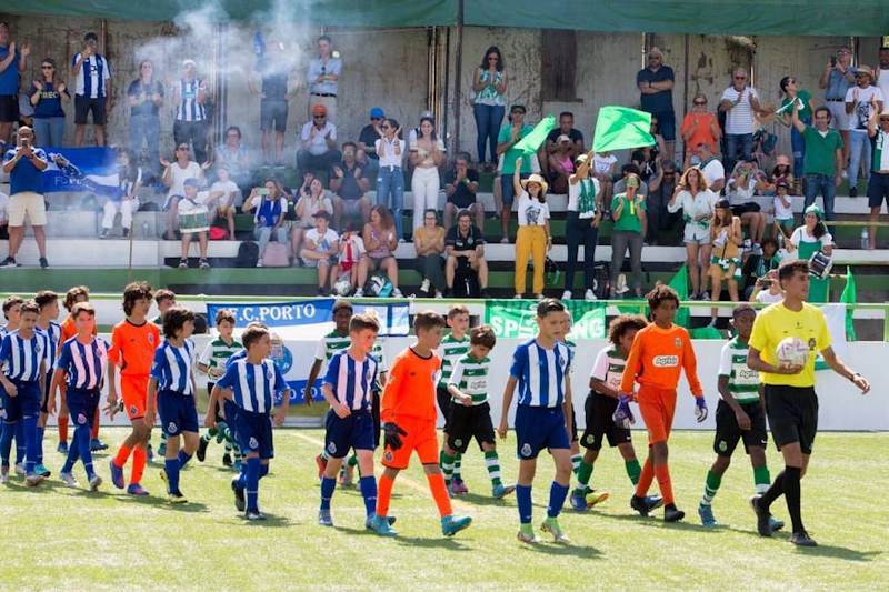 जूनियर फुटबॉल टीमें रेफरी और स्टैंड्स में प्रशंसकों के साथ मिरांडा कप समर टूर्नामेंट में मैदान में चलती हैं।