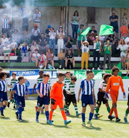 Młodzieżowe drużyny piłkarskie wchodzące na boisko z sędziami i kibicami na letnim turnieju Miranda Cup.