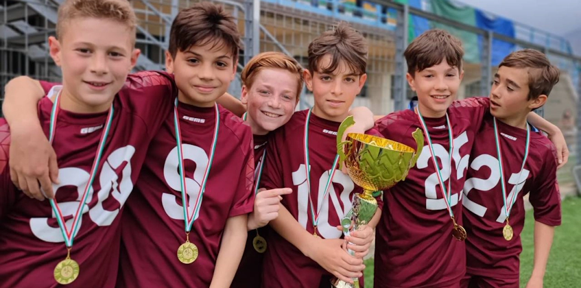 Young soccer players in maroon jerseys with medals and a trophy on the football pitch