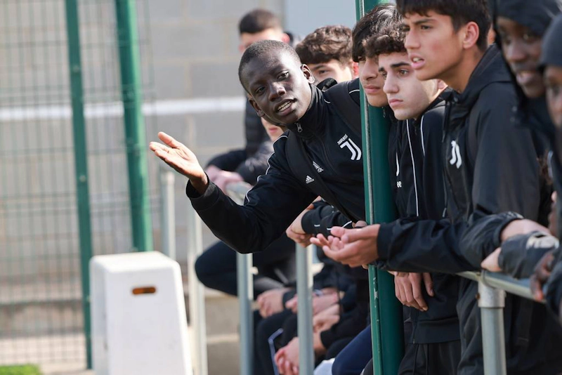 Młodzi piłkarze w dresach Juventus skupieni na grze, jeden z nich gestykuluje wyjaśniająco.
