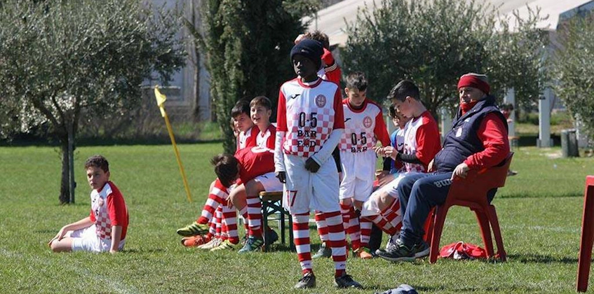Youth football players in red and white kits rest and strategize on the bench during a game.