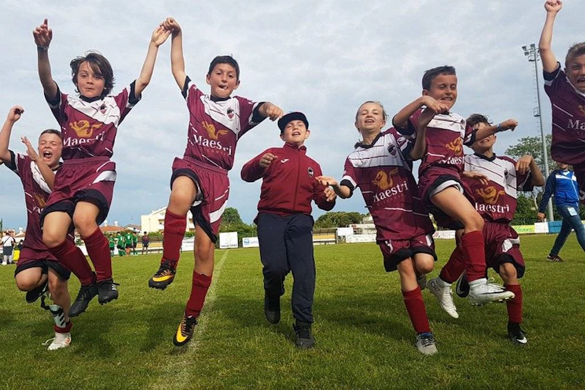 Youth football team joyfully jumping in maroon kits on the field at the Venezia Jesolo Cup
