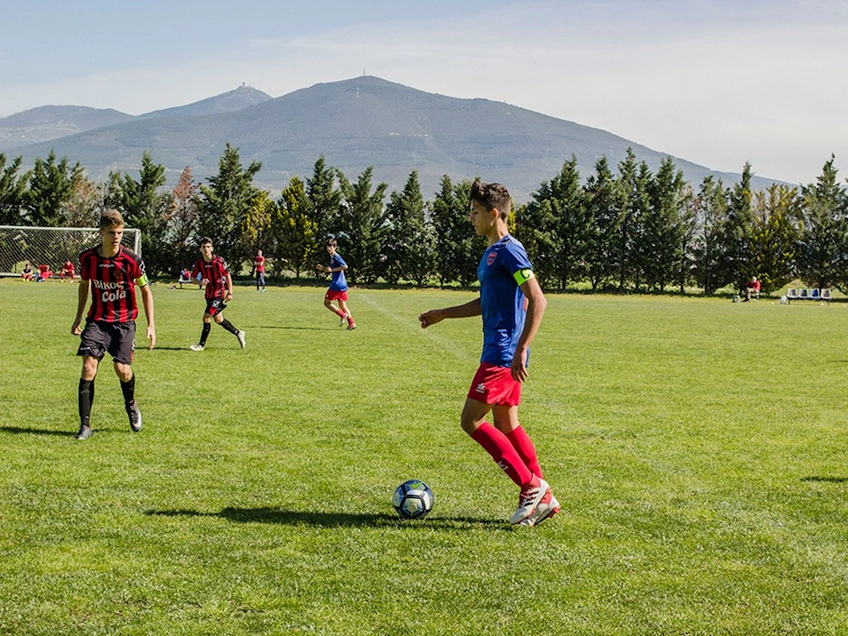 Unge fodboldspillere spiller ved Salonica Soccer Cup med bjerge i baggrunden