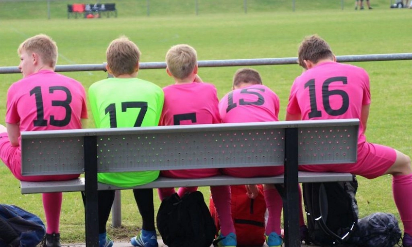 鮮やかなピンクのユニフォームを着たユースサッカーチームがベンチに座っている
