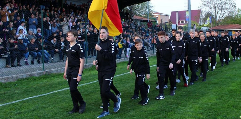 Nuori jalkapallojoukkue marssii stadionilla lipun kanssa