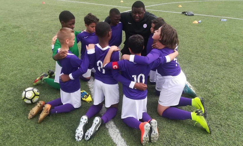 Youth soccer team in huddle on field with coach