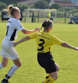 Two female footballers in a match, one in white and the other in yellow, competing for the ball on a green pitch.