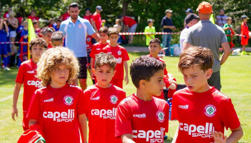 Jovens jogadores de futebol em uniformes vermelhos andando no campo no torneio Pyrenees Cup.