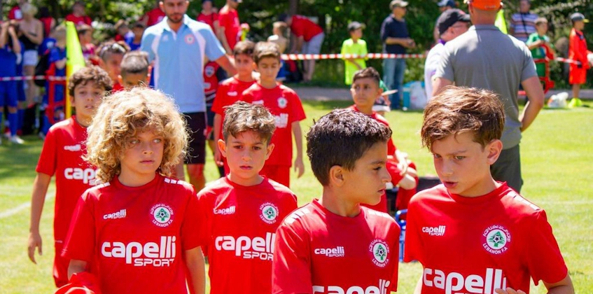 Tineri fotbaliști în uniforme roșii merg pe teren la turneul Pyrenees Cup.