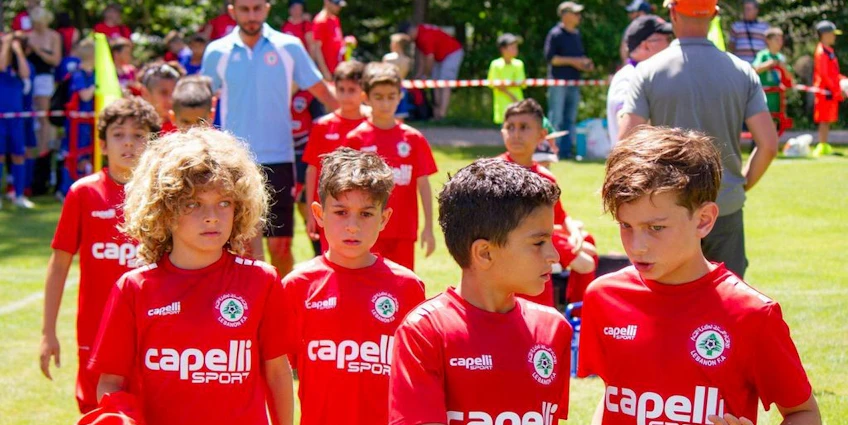 年轻的足球运动员身穿红色制服，在比利牛斯杯足球赛上走在场地上。