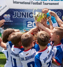 Antrenorul și tinerii fotbaliști ridică un trofeu la turneul Cupa Juniorilor