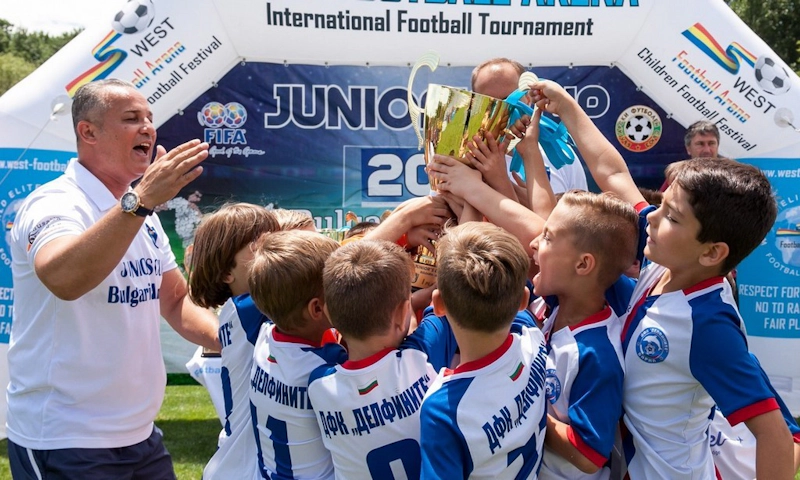 Træner og unge fodboldspillere løfter et trofæ ved Junior's Cup turneringen