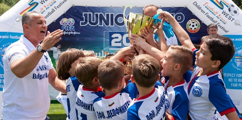 Coach en jonge voetballers tillen een trofee op bij het Junior's Cup toernooi